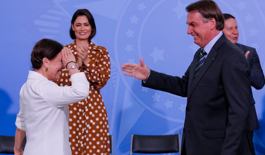 Em cerimônia de posse como secretária da cultura, Regina Duarte bate continência para Jair Bolsonaro, que estende a mão para cumprimentá-la. Ao fundo, a primeira-dama e o vice-presidente.